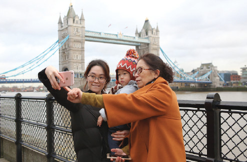 Three Chinese tourists pose for a selfie next to the River Thames in London